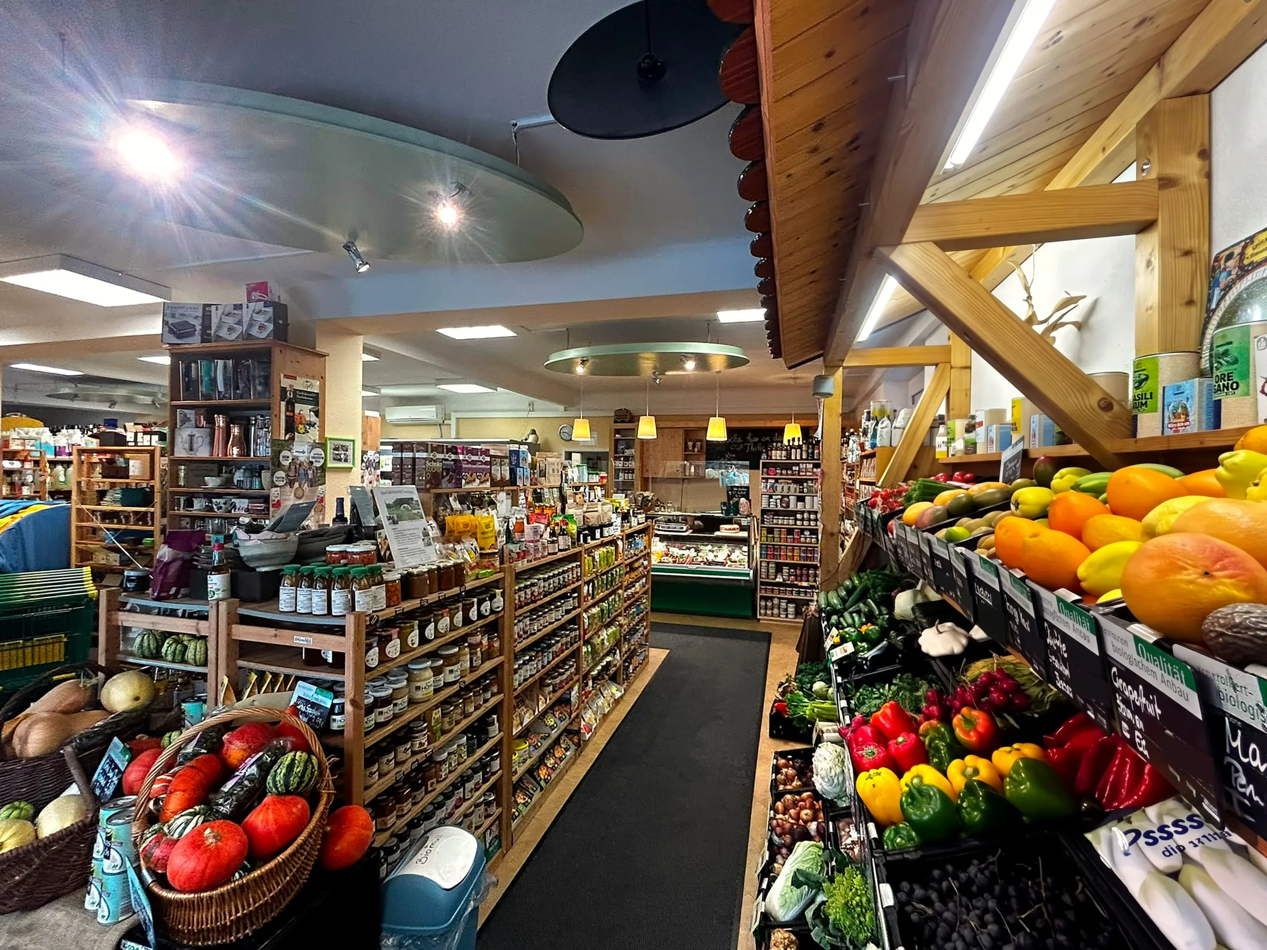 Blick in den Biolino Naturmarkt: Obst- und Gemüseauslage unter Holzgebälk, dahinter Regale und Theke